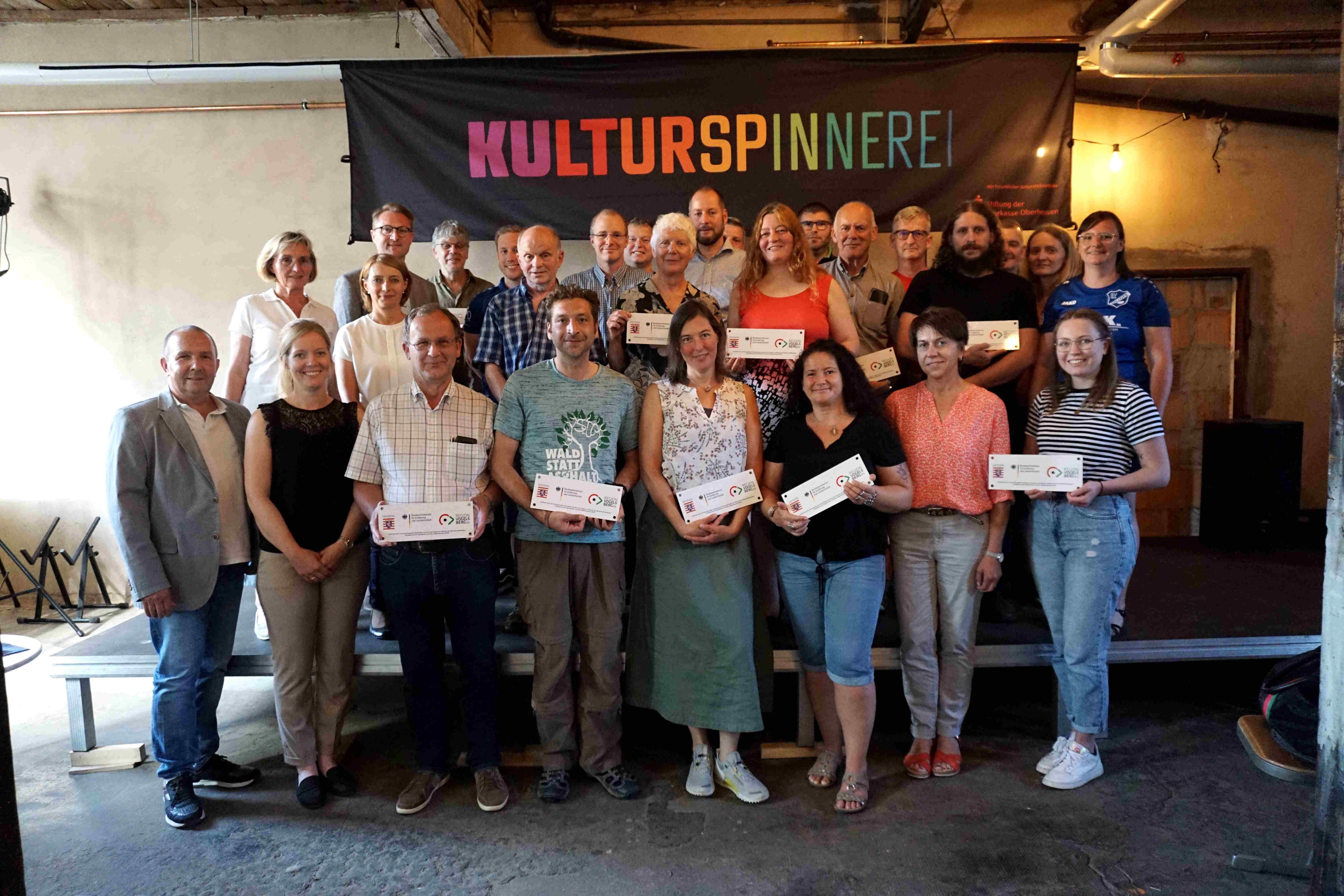  Die Plaketten, die bares Geld wert sind: Dr. Jens Mischak (hintere Reihe links), gemeinsam mit den Vertreterinnen und Vertretern Vogelsberger Vereine, die in der Lauterbacher Kulturspinnerei die Regionalbudget-Plaketten präsentieren. Zuständig für Beratung und Vergabe sind Matthias Steckenreuther (vorne von links), Jennifer Berger, Verein Region Vogelsberg, Christel Hensel (zweite Reihe von links), stellvertretende Vorsitzende des LEADER-Entscheidungsgremiums sowie Tatjana Heinz vom Verein Region Vogelsberg. 