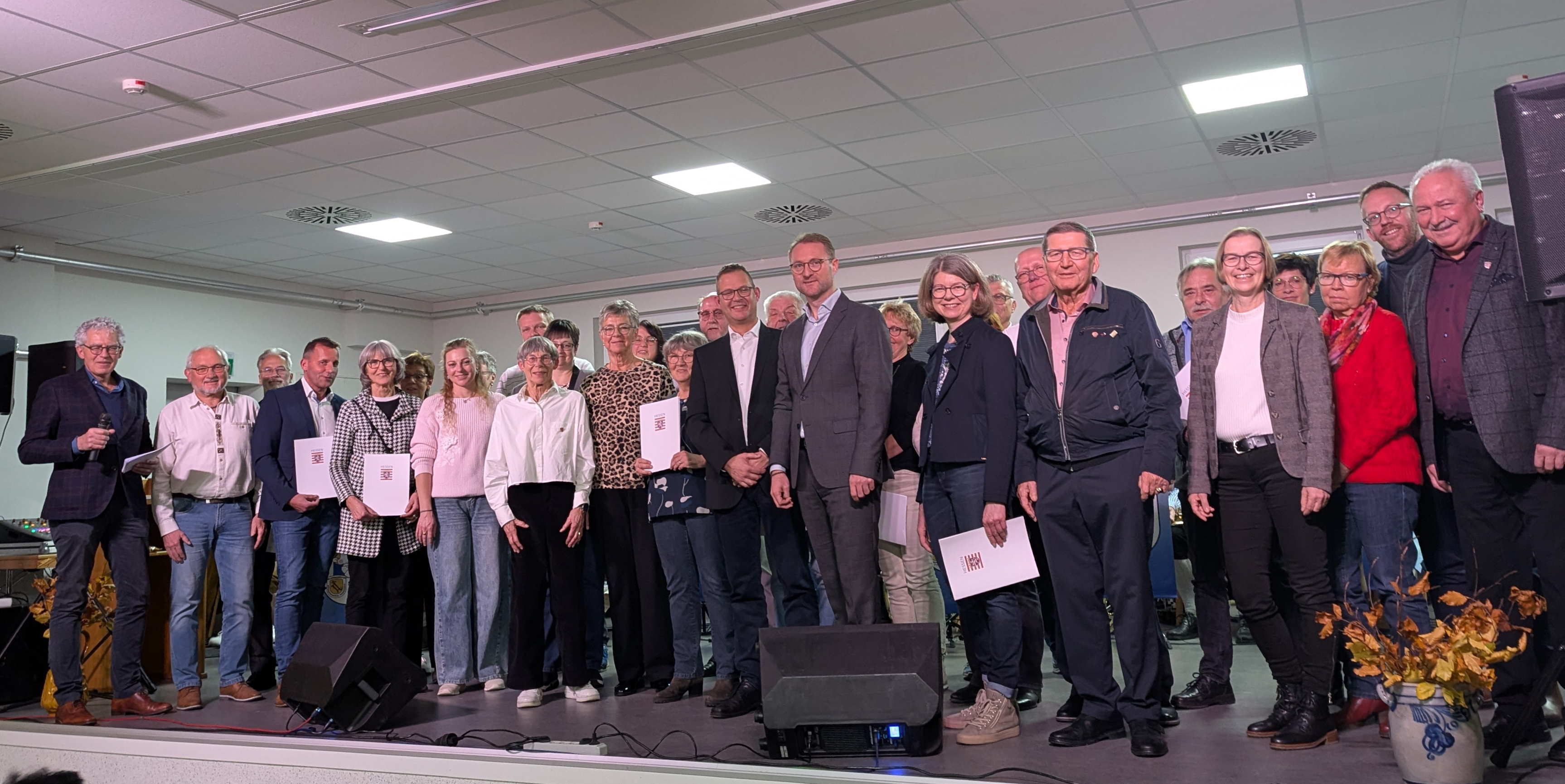 Gruppenbild mit Vertreterinnen und Vertretern der teilnehmenden Dörfer gemeinsam mit Landrat Dr. Jens Mischak (vorne, Siebter von rechts), Barbara Eckhardt (vorne, Sechste von links), Kreisbeigeordnete des Landkreises Hersfeld-Rotenburg, Schwalmtals Bürgermeister Timo Georg (vorne, Achter von rechts) und Lorenz Kock (links), Leiter des Amtes für Wirtschaft und den ländlichen Raum des Vogelsbergkreises, zum Abschluss der Siegerehrung des 38. Regionalwettbewerbs im Dorfgemeinschaftshaus des Siegerdorfs Storndorf.