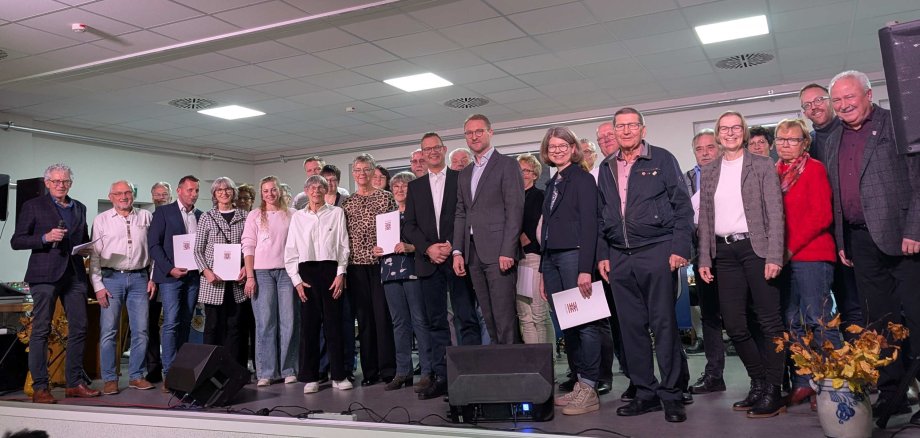 Gruppenbild mit Vertreterinnen und Vertretern der teilnehmenden Dörfer gemeinsam mit Landrat Dr. Jens Mischak (vorne, Siebter von rechts), Barbara Eckhardt (vorne, Sechste von links), Kreisbeigeordnete des Landkreises Hersfeld-Rotenburg, Schwalmtals Bürgermeister Timo Georg (vorne, Achter von rechts) und Lorenz Kock (links), Leiter des Amtes für Wirtschaft und den ländlichen Raum des Vogelsbergkreises, zum Abschluss der Siegerehrung des 38. Regionalwettbewerbs im Dorfgemeinschaftshaus des Siegerdorfs Storndorf.