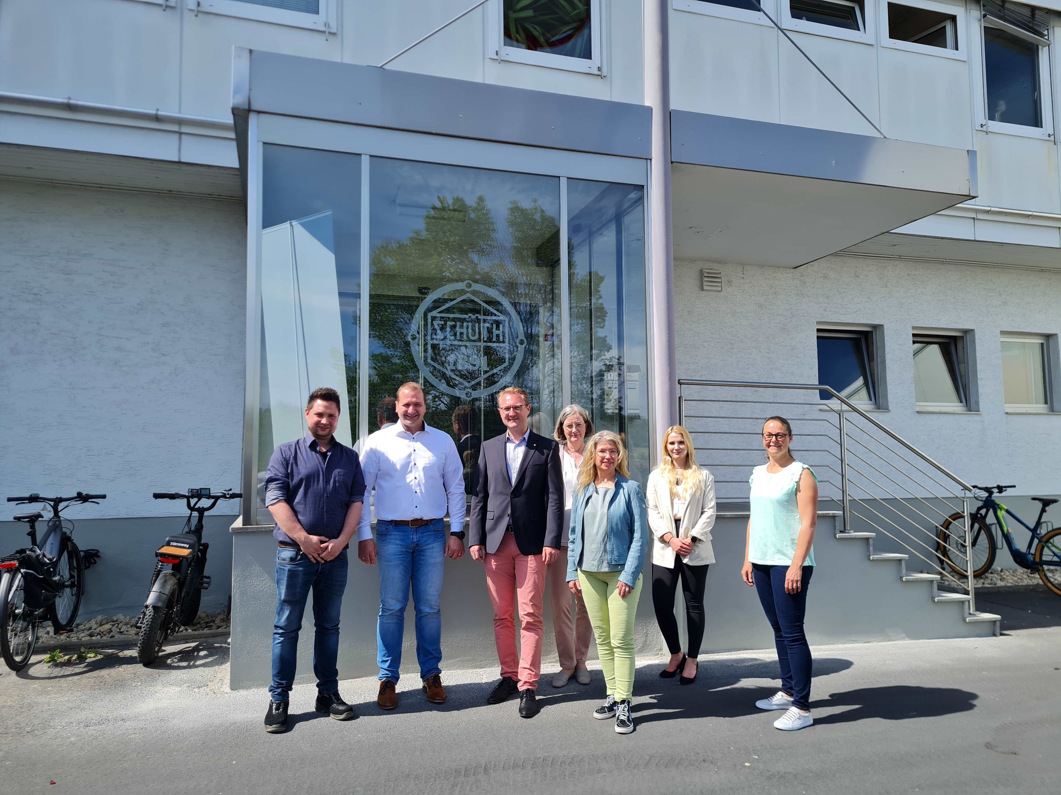 Sieben Menschen haben sich vor einem Gebäudeeingang zum Gruppenbild aufgestellt. Dr. Jens Mischak (Dritter von links), Erster Kreisbeigeordneter und Wirtschaftsdezernent, gemeinsam mit Betriebsleiter und Prokurist Samuel Hess (von links), Geschäftsführer Kai Kloske, Andrea Ortstadt von der Wirtschaftsförderung, Susanne Schaab, Bürgermeisterin der Stadt Schotten, Annabel Ziepf, Kaufmännischen Leiterin und Prokuristin bei Schüth sowie Susen Neumann, Arbeitgeberservice der KVA Vogelsbergkreis sind darauf zu sehen.