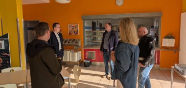 Fünf Personen stehen in einer Schul-Cafeteria im Kreis und sprechen miteinander