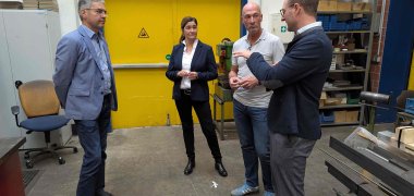 Gespräch in der Holzwerkstatt. Vier Menschen stehen im Halbkreis und sprechen miteinander. 