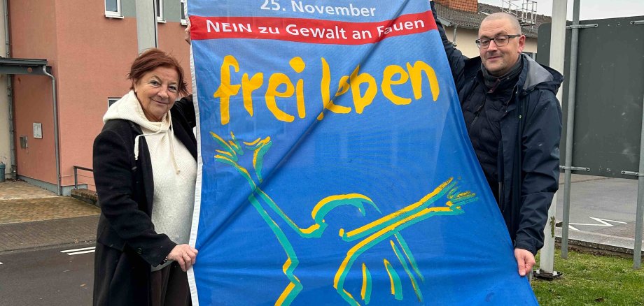 Elisabeth Hillebrand, Beauftragte für Integration und Gleichstellung, gemeinsam mit Bastian Heck, Leiter des Sachgebiets Soziale Dienste im Amt für Soziales und Ausländerrecht, mit der Fahne des Vereins „Terre des Femmes“, die unter dem Motto „NEIN zu Gewalt an Frauen! – Frei leben ohne Gewalt“ auf den internationalen Tag gegen Gewalt an Frauen aufmerksam macht.