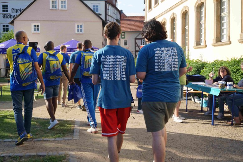 Zwei junge Menschen laufen mit blauen Tshirts bekleidet durch das Bild. Darauf ist Inklusionstag zu lesen