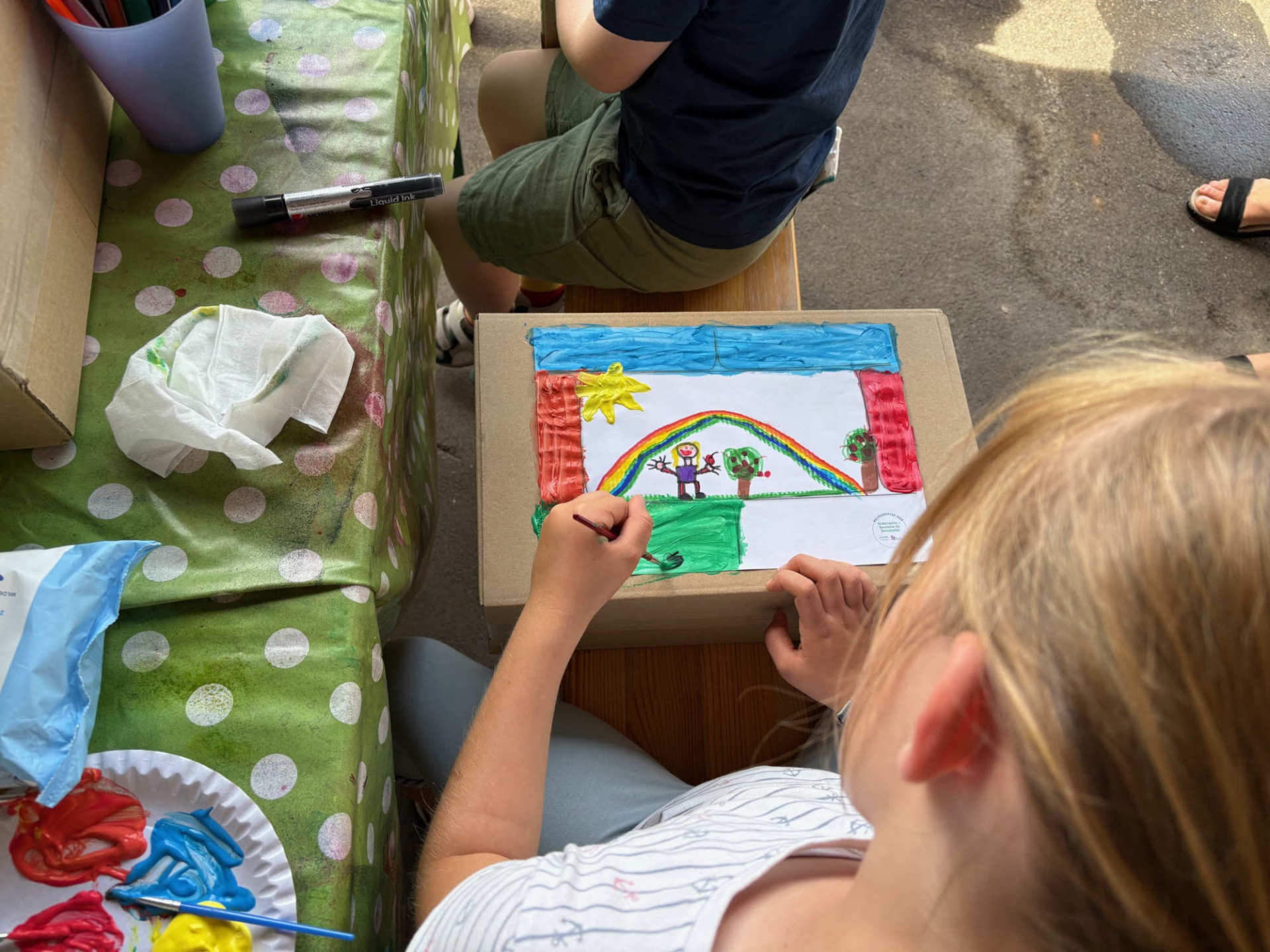 ein Kind malt mit Wasserfarben ein Bild auf einen Karton
