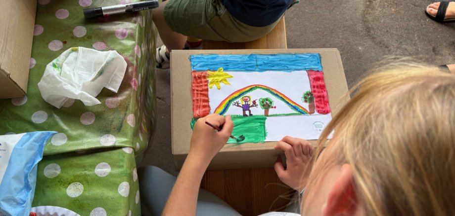 ein Kind malt mit Wasserfarben ein Bild auf einen Karton