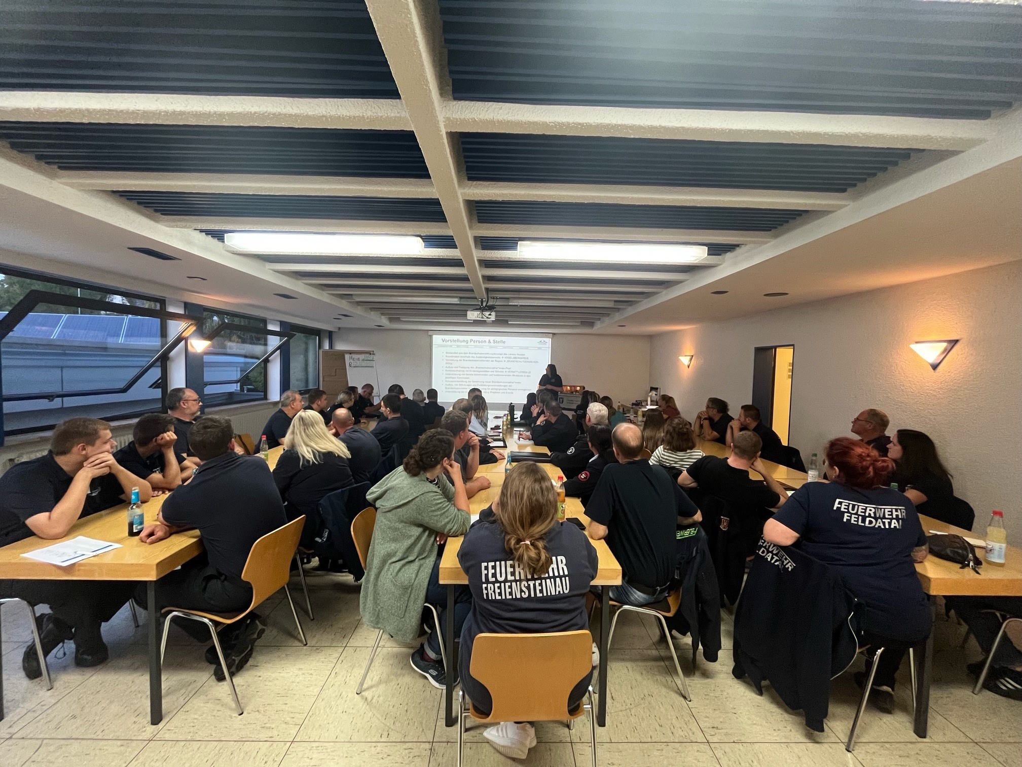 an drei langen Tischreihen sitzen knapp 60 Menschen und lauschen einem Vortrag zu Brandschutzerziehung bei Kindern