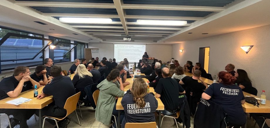 an drei langen Tischreihen sitzen knapp 60 Menschen und lauschen einem Vortrag zu Brandschutzerziehung bei Kindern