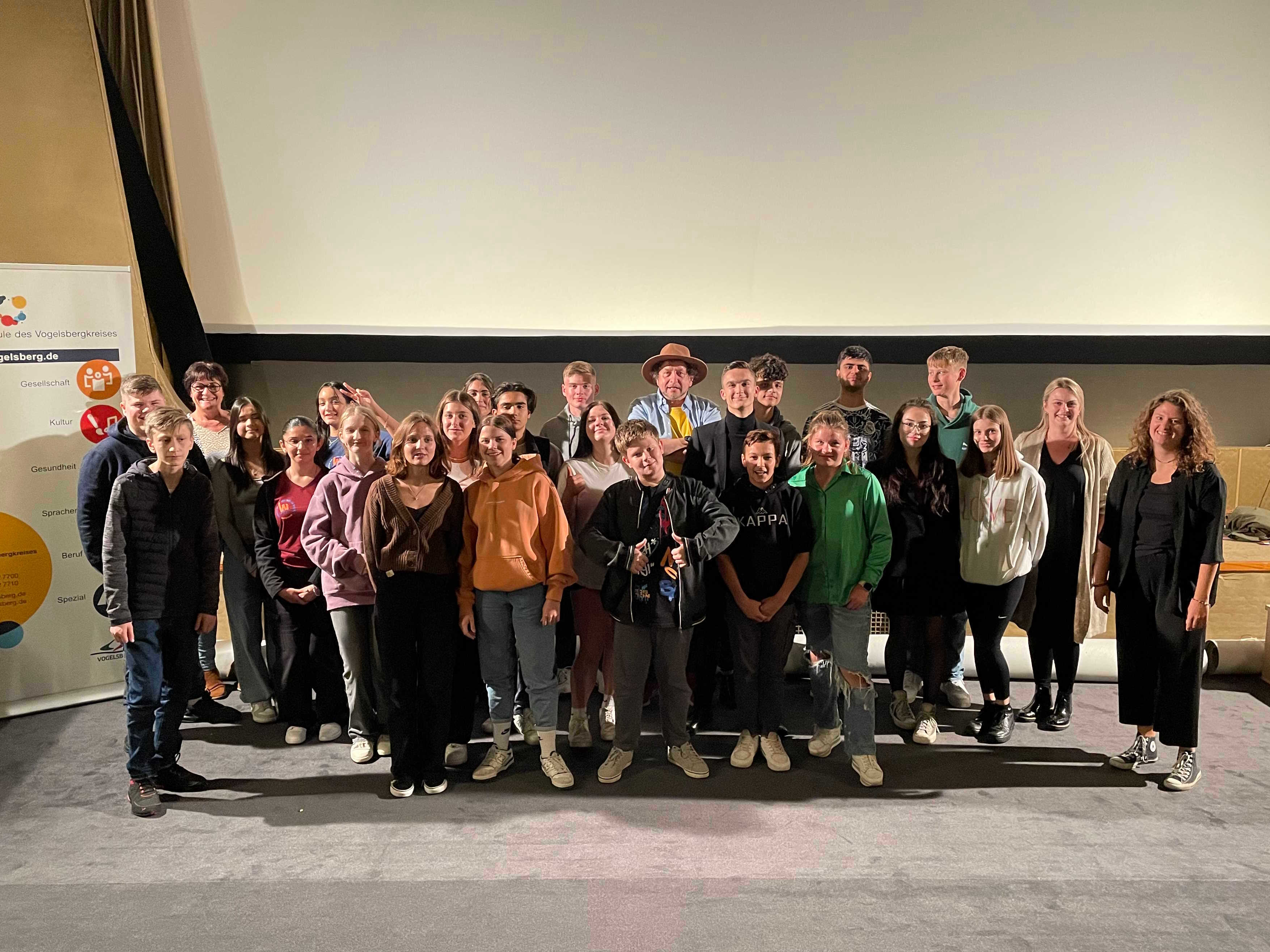 Vor einer Kinoleinwand haben sich rund 30 Menschen für ein Gruppenfoto aufgestellt. 