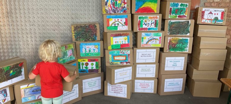 Ein kleines Kind steht vor einer Wand aus bunt bemalten Kartons