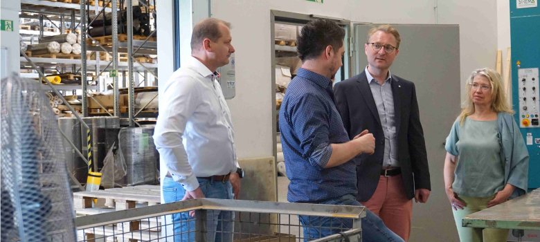 vier Menschen stehen in einer Industriehalle und sprechen über Stanzteile