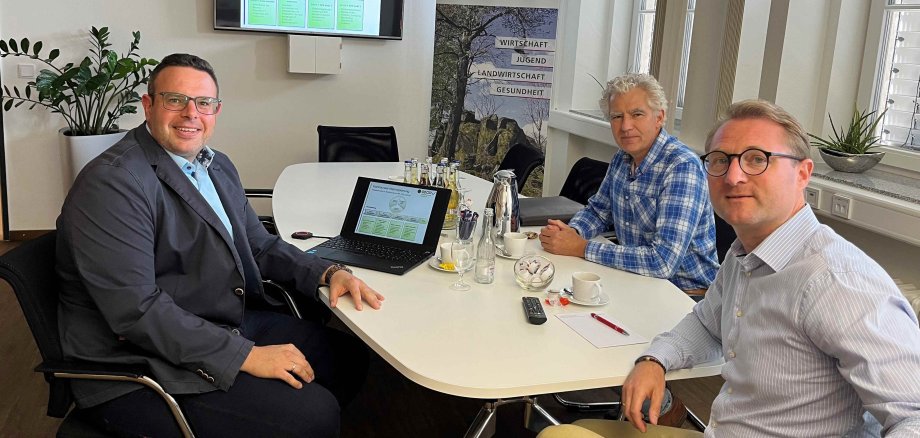 Björn Köhler (links), Erster Kreisbeigeordneter Dr. Jens Mischak (Mitte) und der Leiter der Wirtschaftsförderung der Kreisverwaltung, Lorenz Kock sitzen an einem Konferenztisch und schauen in die Kamera