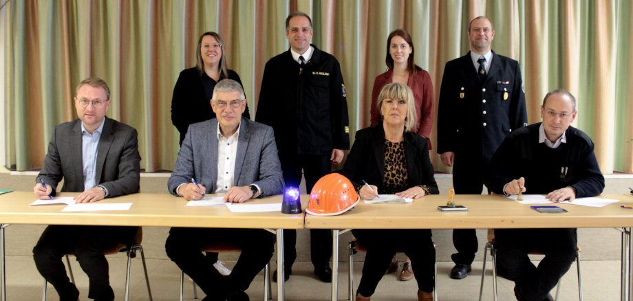   Landrat Manfred Görig (sitzend, Zweiter von links) und Erster Kreisbeigeordneter Dr. Jens Mischak (links) unterzeichnen gemeinsam mit Andrea Wolf, Leiterin der Oberwaldschule und Sebastian Stang, Bürgermeister von Grebenhain, einen Kooperationsvertrag für das Projekt des Wahlpflichtfachs „Feuerwehr“. Auch Brandschutzkoordinatorin des Kreises, Heidi Schmidt, Kreisbrandinspektor Dr. Sven Holland, Lehrerin Angelina Heun und Gemeindebrandinspektor Mario Henning (hinten, von links) freuen sich auf das gemeinsame Projekt in Grebenhain. 