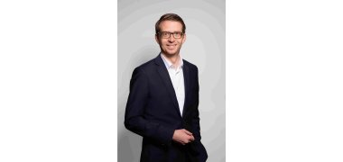 Porträtfoto von Staatssekretär Michael Ruhl. Er trägt eine Brille und lächelt in die Kamera.