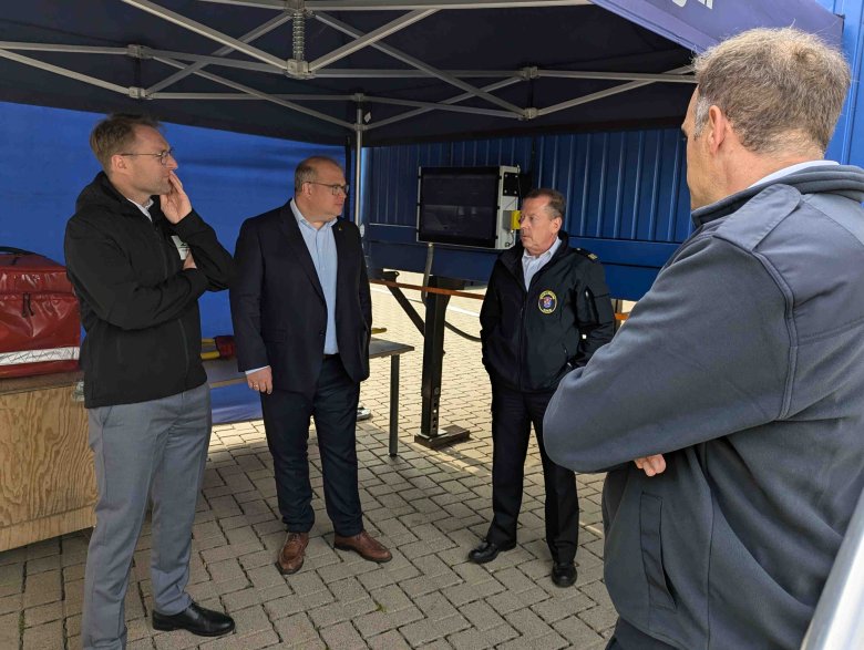 Vier Männer stehen unter einem Zeltpavillion und sprechen über ein Übungsszenario in einem Brandsimulationscontainer