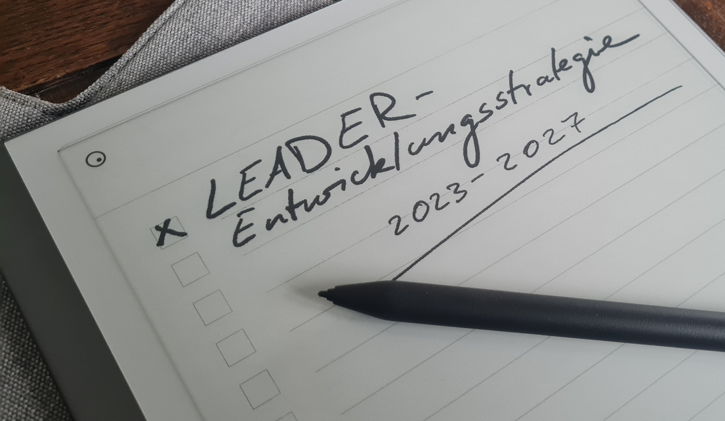 Symbolfoto. ein Tablet liegt auf einem Holztisch. Das Tablet zeigt den handschriftlichen Text LEADER-Entwicklungsstrategie 2023-2027 an. 