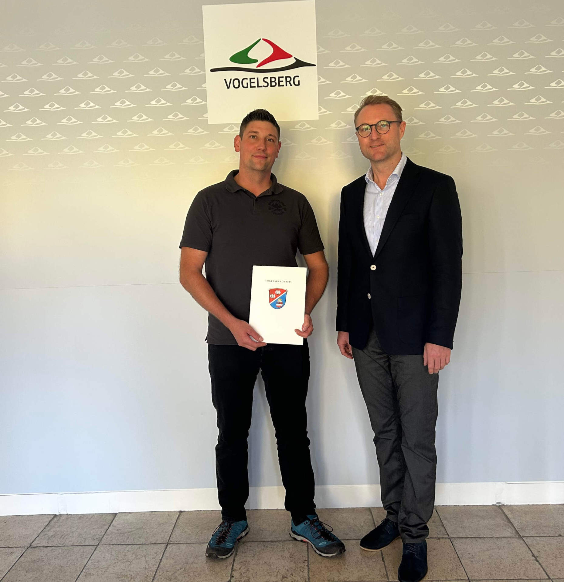 Zwei Männer stehen vor einer Wand und präsentieren einen Förderbescheid.