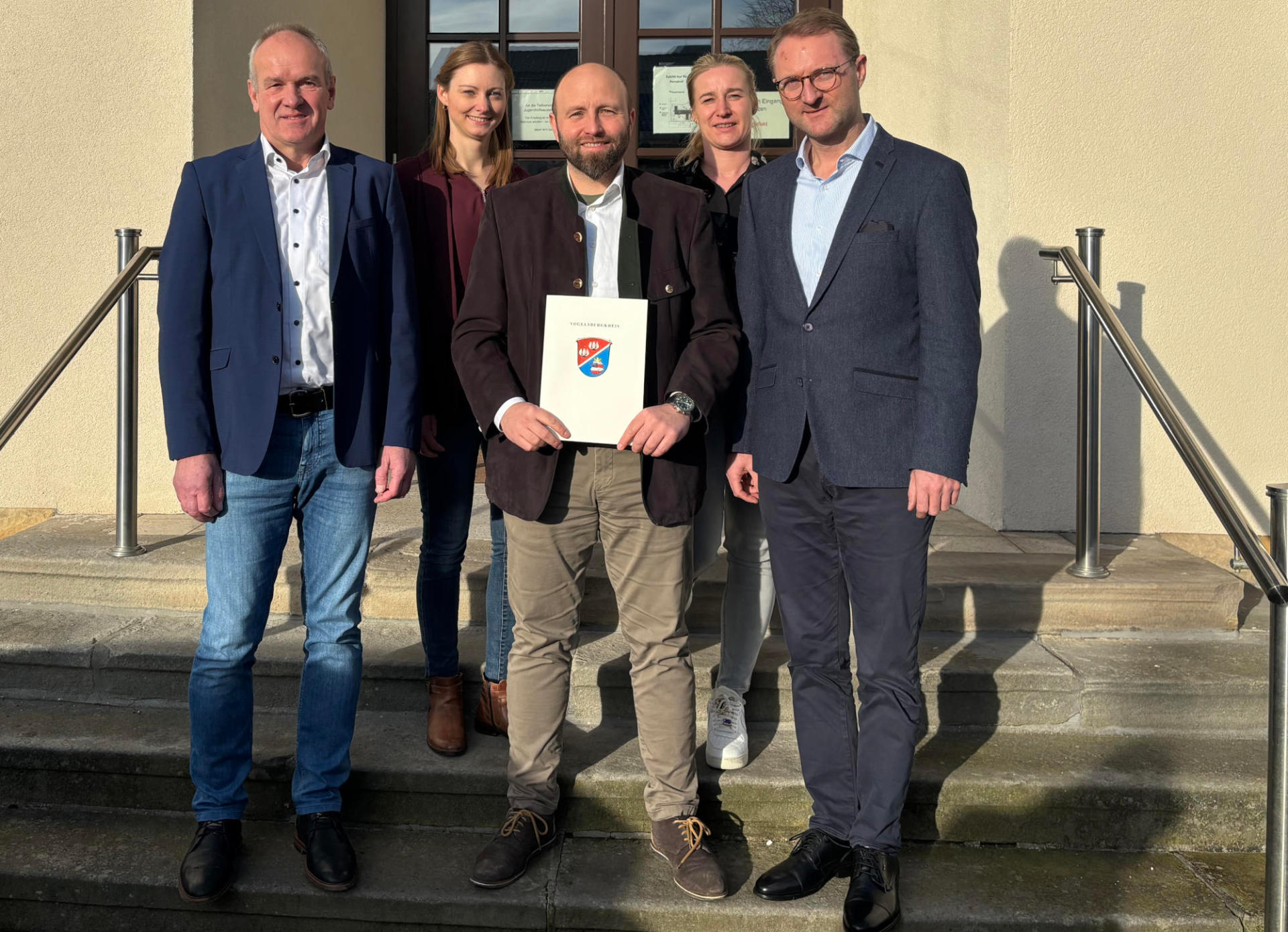 Landrat Dr. Mischak (rechts) übergibt gemeinsam mit dem LEADER-Beiratsvorsitzenden Edwin Schneider (links), Jana Brittner (hinten links), Sachgebietsleitung der Dorf- und Regionalentwicklung im Amt für Wirtschaft und den ländlichen Raum des Vogelsbergkreises, und Katharina Orth vom Verein Region Vogelsberg den Förderbescheid an Schottens Bürgermeister Benjamin Göbl.