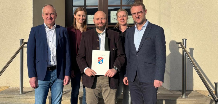Landrat Dr. Mischak (rechts) übergibt gemeinsam mit dem LEADER-Beiratsvorsitzenden Edwin Schneider (links), Jana Brittner (hinten links), Sachgebietsleitung der Dorf- und Regionalentwicklung im Amt für Wirtschaft und den ländlichen Raum des Vogelsbergkreises, und Katharina Orth vom Verein Region Vogelsberg den Förderbescheid an Schottens Bürgermeister Benjamin Göbl.