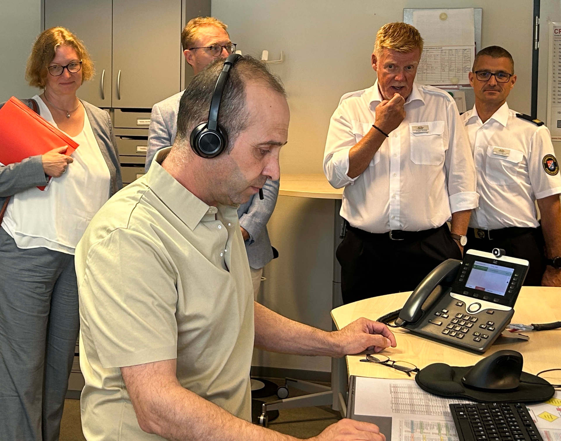Notfall-Dolmetscher Keyvan Seifialou im Einsatz: Am Telefon fragt er gezielt, was der persisch sprechenden Patientin passiert ist, er will wissen, ob sie Schmerzen hat und wie das Allgemeinbefinden ist. Die Informationen gibt er weiter an den Disponenten der Leitstelle, der den Rettungswagen losschickt. Beobachtet wird die Szene von Staatssekretärin Katrin Hechler, Landrat Dr. Jens Mischak, Jürgen Schad, stellvertretender Leiter des Amtes für Gefahrenabwehr, und Kreisbrandinspektor Marcell Büttner (von links).