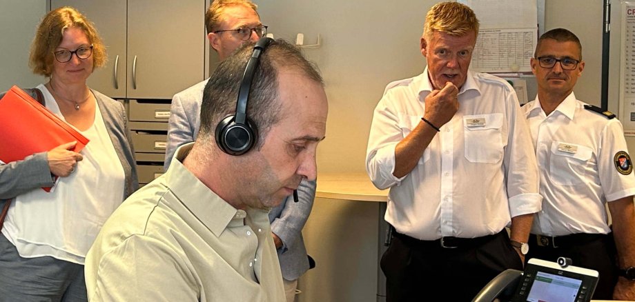 Notfall-Dolmetscher Keyvan Seifialou im Einsatz: Am Telefon fragt er gezielt, was der persisch sprechenden Patientin passiert ist, er will wissen, ob sie Schmerzen hat und wie das Allgemeinbefinden ist. Die Informationen gibt er weiter an den Disponenten der Leitstelle, der den Rettungswagen losschickt. Beobachtet wird die Szene von Staatssekretärin Katrin Hechler, Landrat Dr. Jens Mischak, Jürgen Schad, stellvertretender Leiter des Amtes für Gefahrenabwehr, und Kreisbrandinspektor Marcell Büttner (von links).