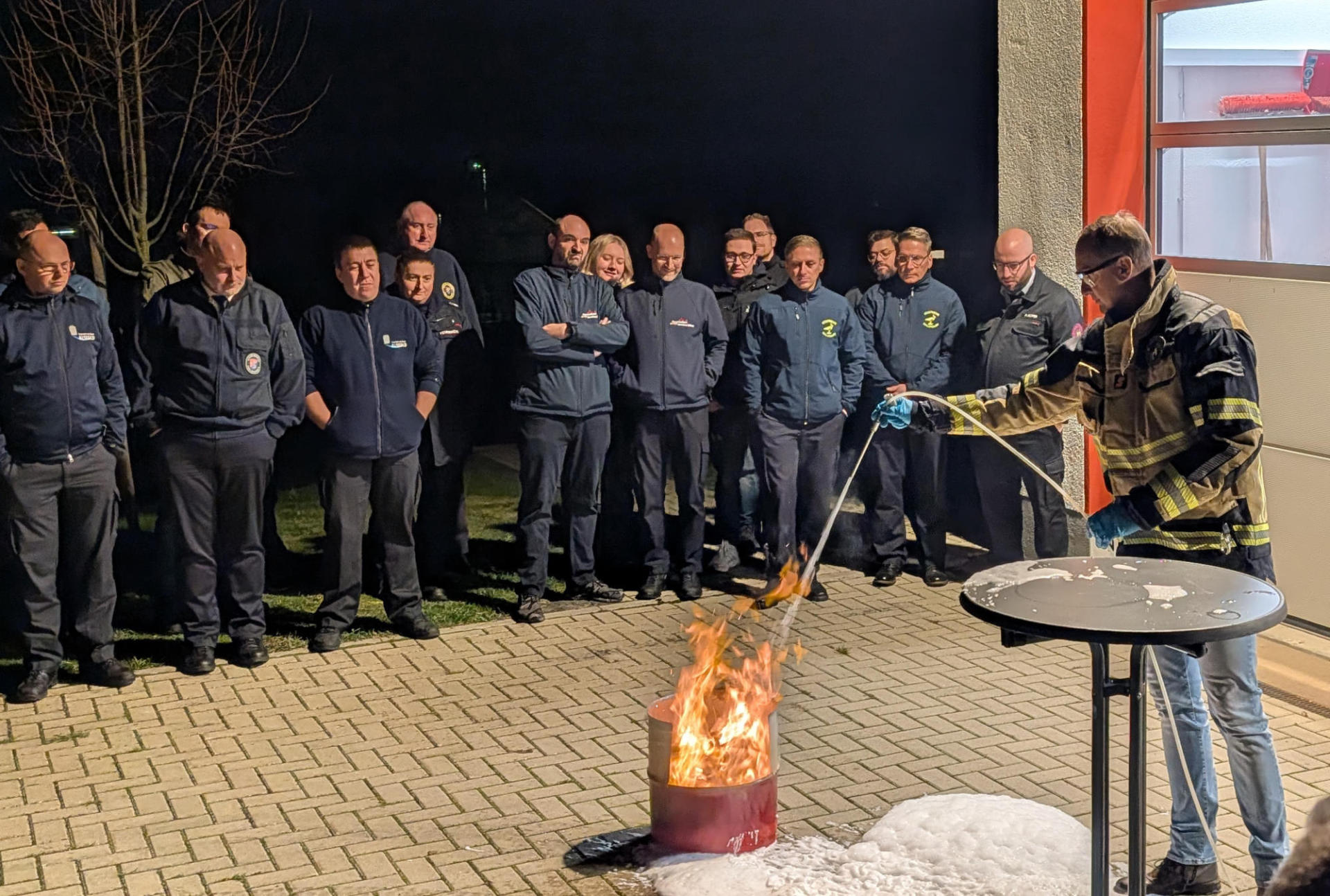 Feuerwehrleute stehen an einer Übungsfeuerstelle und erhalten eine Unterweisung im Löschen mit Schaum.