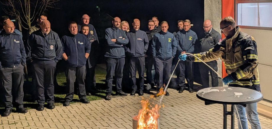 Feuerwehrleute stehen an einer Übungsfeuerstelle und erhalten eine Unterweisung im Löschen mit Schaum.