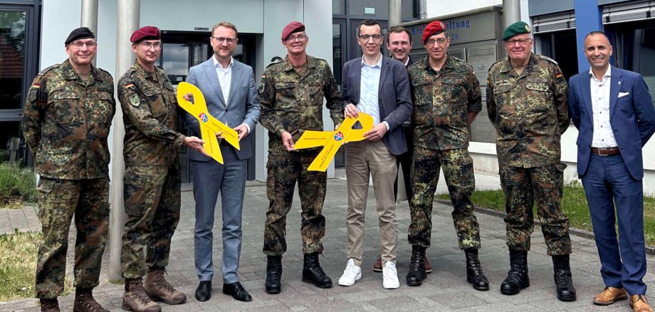 Neun Männer haben sich vor einem Eingang für ein Gruppenbild aufgestellt. Sie präsentieren zwei gelbe Schilder, die Solidarität mit Soldaten zum Ausdruck bringen. Fünf Männer tragen Uniform.