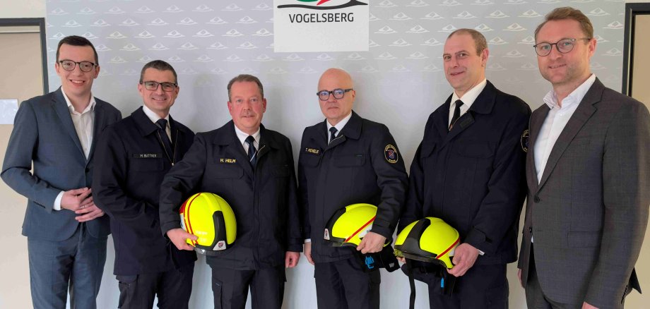 Sechs Männer haben sich zum Gruppenbild aufgestellt. Vier von ihnen tragen Feuerwehruniform. 