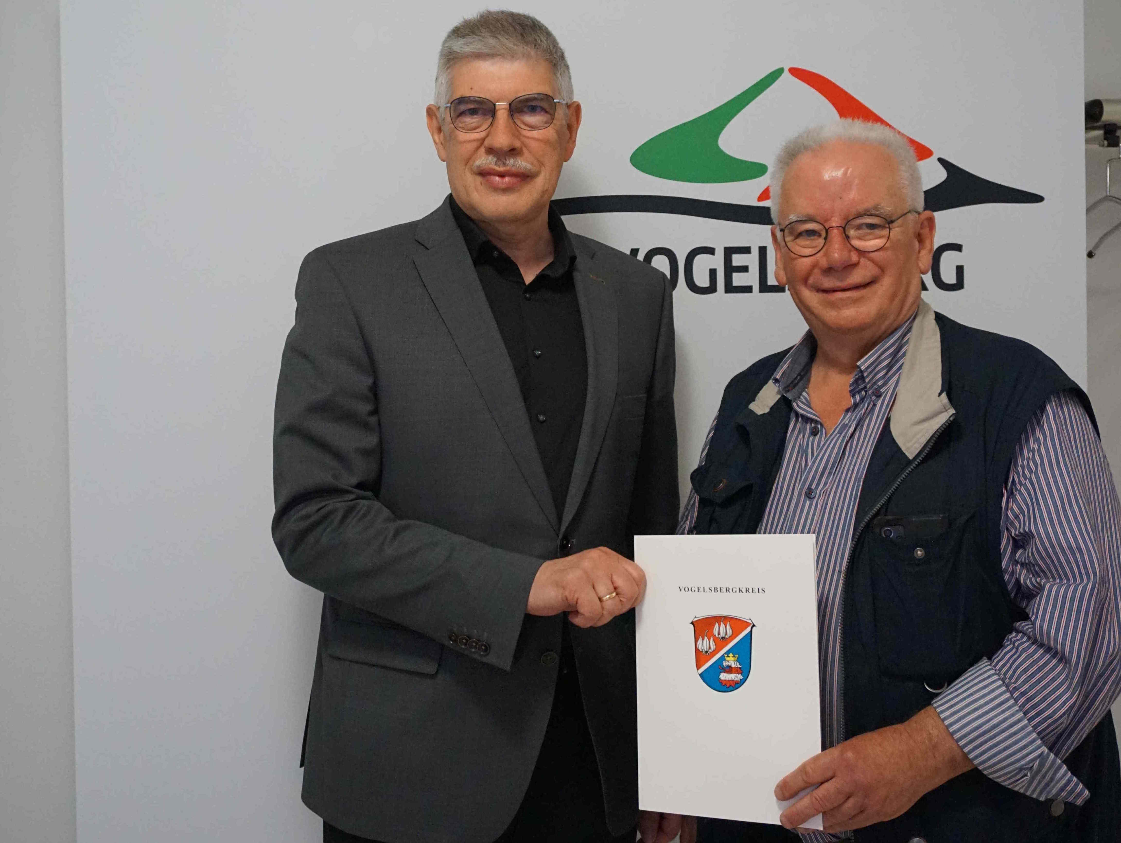 Landrat Manfred Görig und Michael Hermann sind auf dem Foto zu sehen. Sie halten gemeinsam eine Urkunde in der Hand