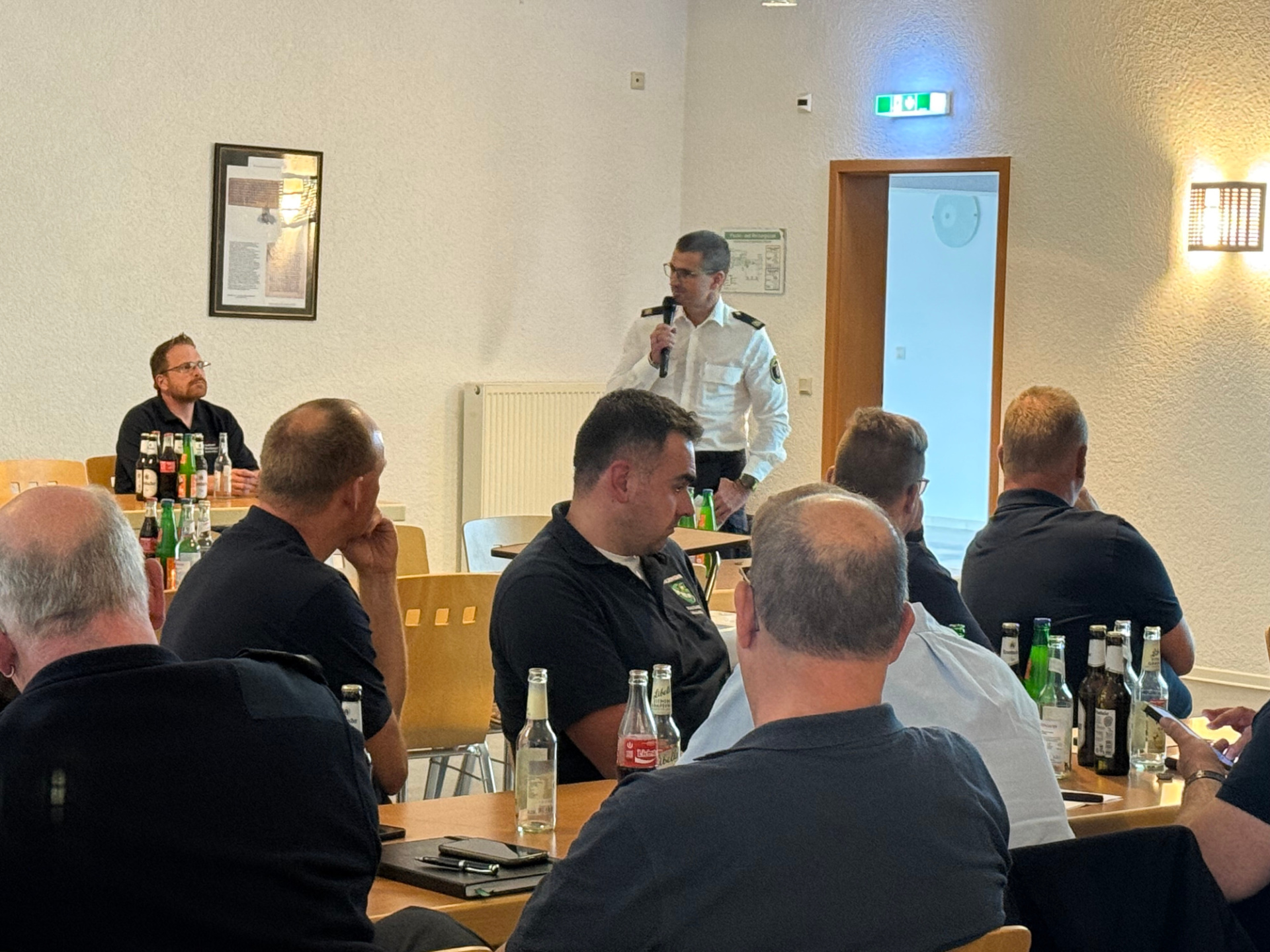 Ein Mann spricht mit Mikrofon in einem Bürgerhaus vor einer Gruppe von Menschen. 