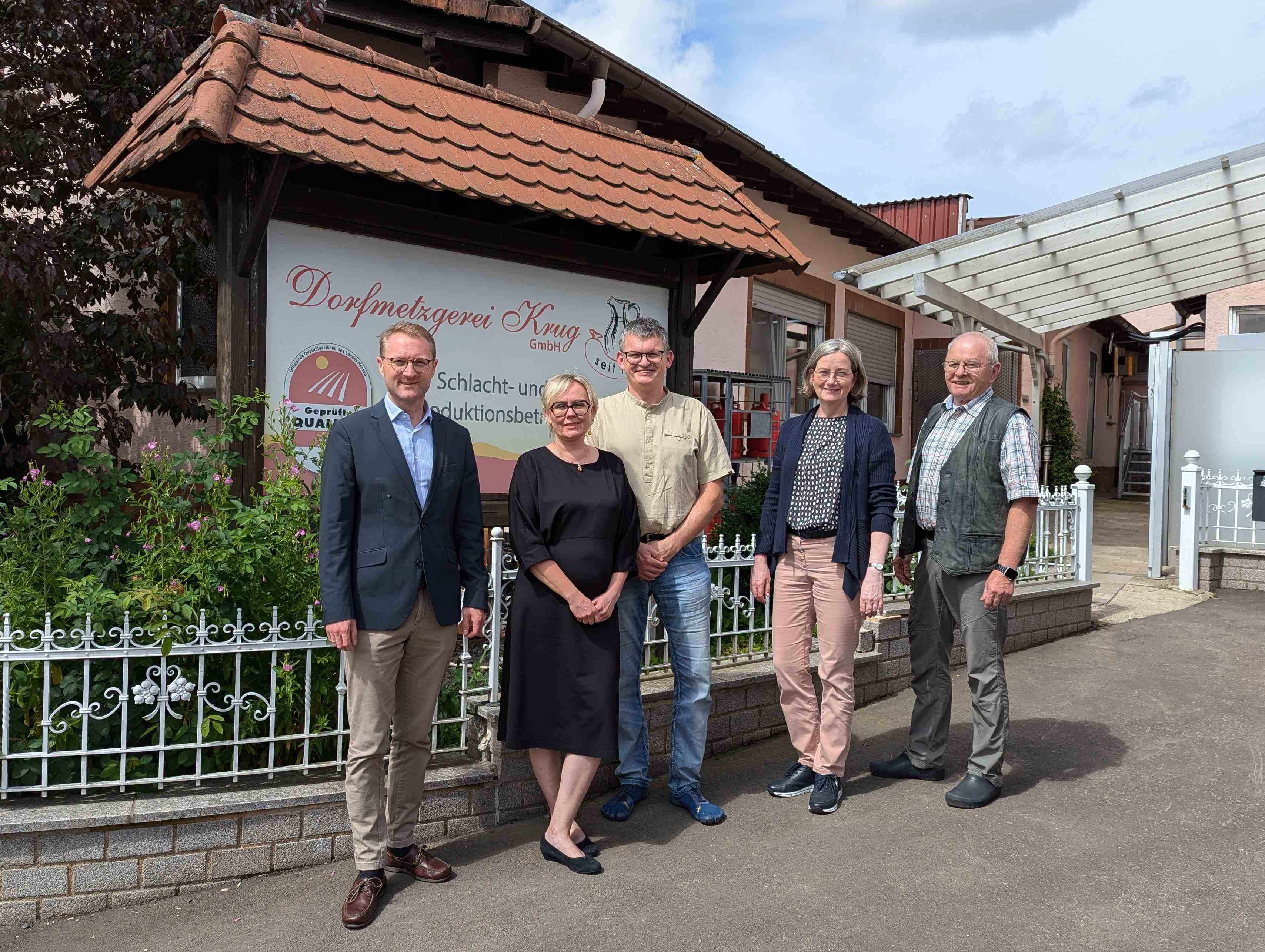 Landrat und Wirtschaftsdezernent Dr. Jens Mischak (links), und Andrea Ortstadt (Zweite von rechts), Wirtschaftsförderung des Vogelsbergkreises, vor dem Produktionsstandort in Brauerschwend. Kai Döring (Mitte), Metzgermeister und Inhaber der Dorfmetzgerei Krug, stellt dort gemeinsam mit seinem Vater Volker Döring und seiner Ehefrau Aneta Döring, die im Betrieb mitarbeiten, die Dorfmetzgerei und ihr besonderes Betriebsmodell vor.