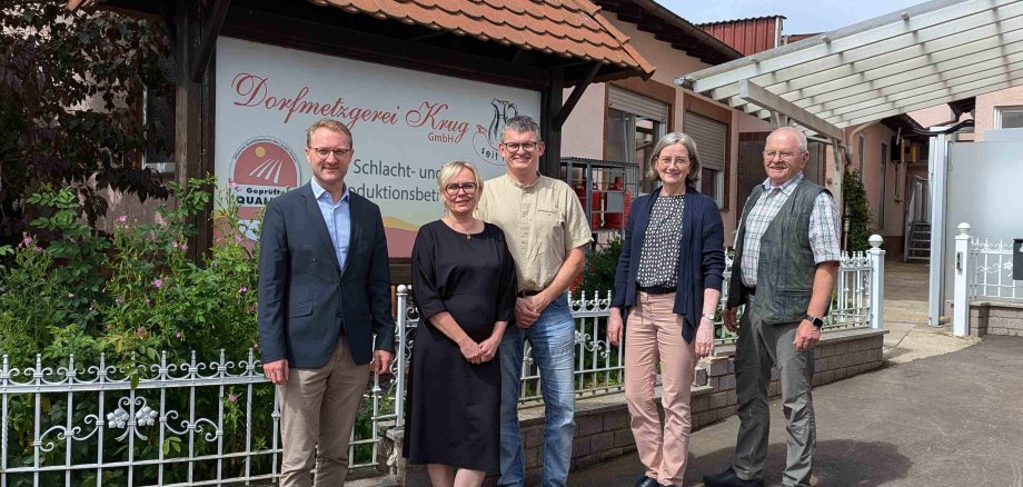 Landrat und Wirtschaftsdezernent Dr. Jens Mischak (links), und Andrea Ortstadt (Zweite von rechts), Wirtschaftsförderung des Vogelsbergkreises, vor dem Produktionsstandort in Brauerschwend. Kai Döring (Mitte), Metzgermeister und Inhaber der Dorfmetzgerei Krug, stellt dort gemeinsam mit seinem Vater Volker Döring und seiner Ehefrau Aneta Döring, die im Betrieb mitarbeiten, die Dorfmetzgerei und ihr besonderes Betriebsmodell vor.