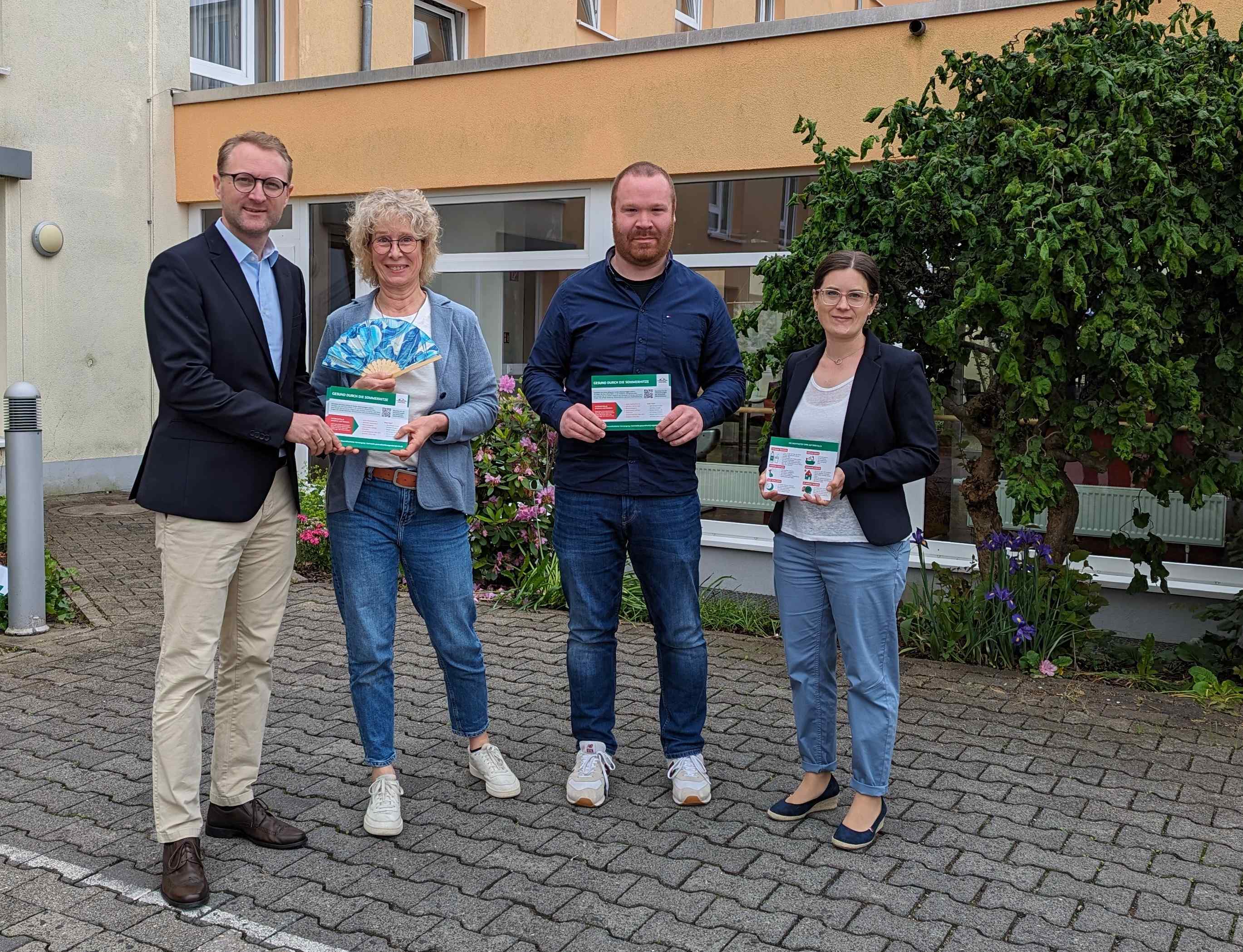 Gesundheitsdezernent Dr. Mischak überreicht bei einem Vor-Ort-Termin im AWO Sozialzentrum Lauterbach nfoflyer an Einrichtungsleiterin Sylvia Motz-Sattler und Pflegedienstleiter Christoph von Keitz. Sie stehen vor gemeinsam mit Carina Diezemann vor dem Gebäude.