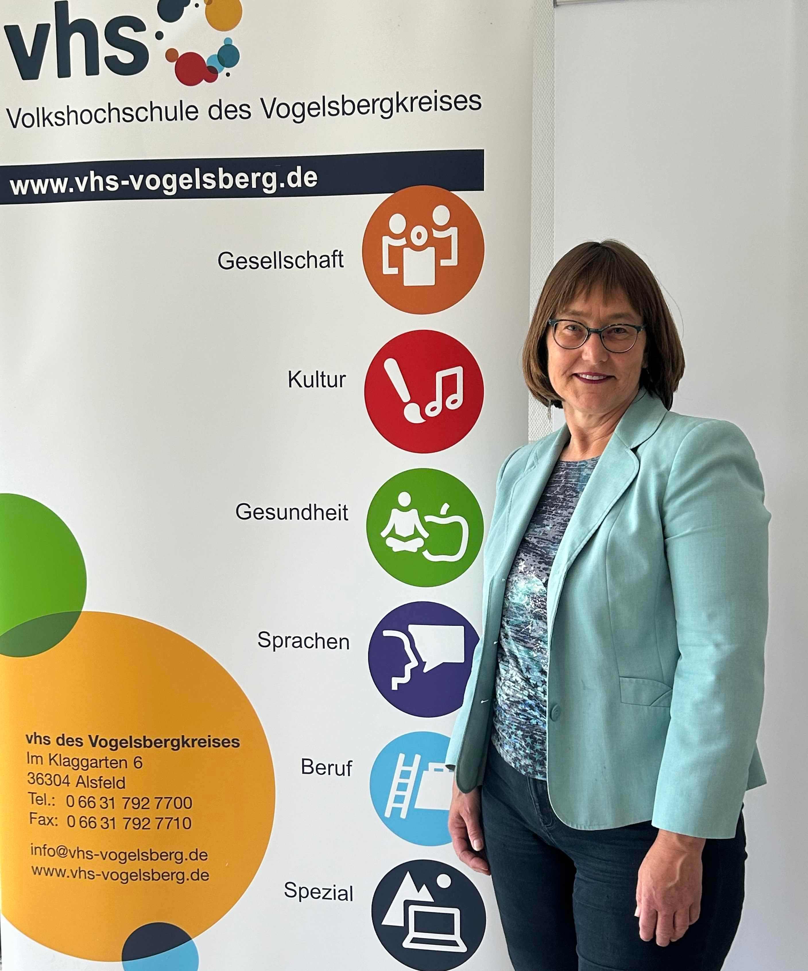 Monika Schenker, Leiterin der Volkshochschule, steht vor einem Plakat, das für die vhs wirbt.