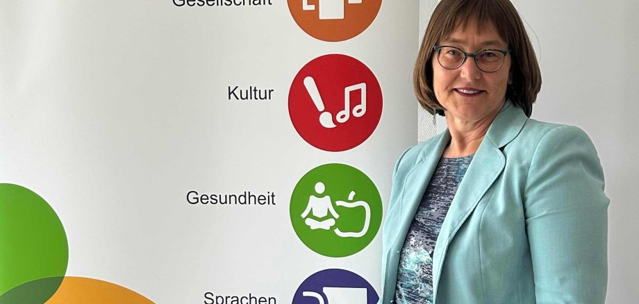 Monika Schenker, Leiterin der Volkshochschule, steht vor einem Plakat, das für die vhs wirbt.