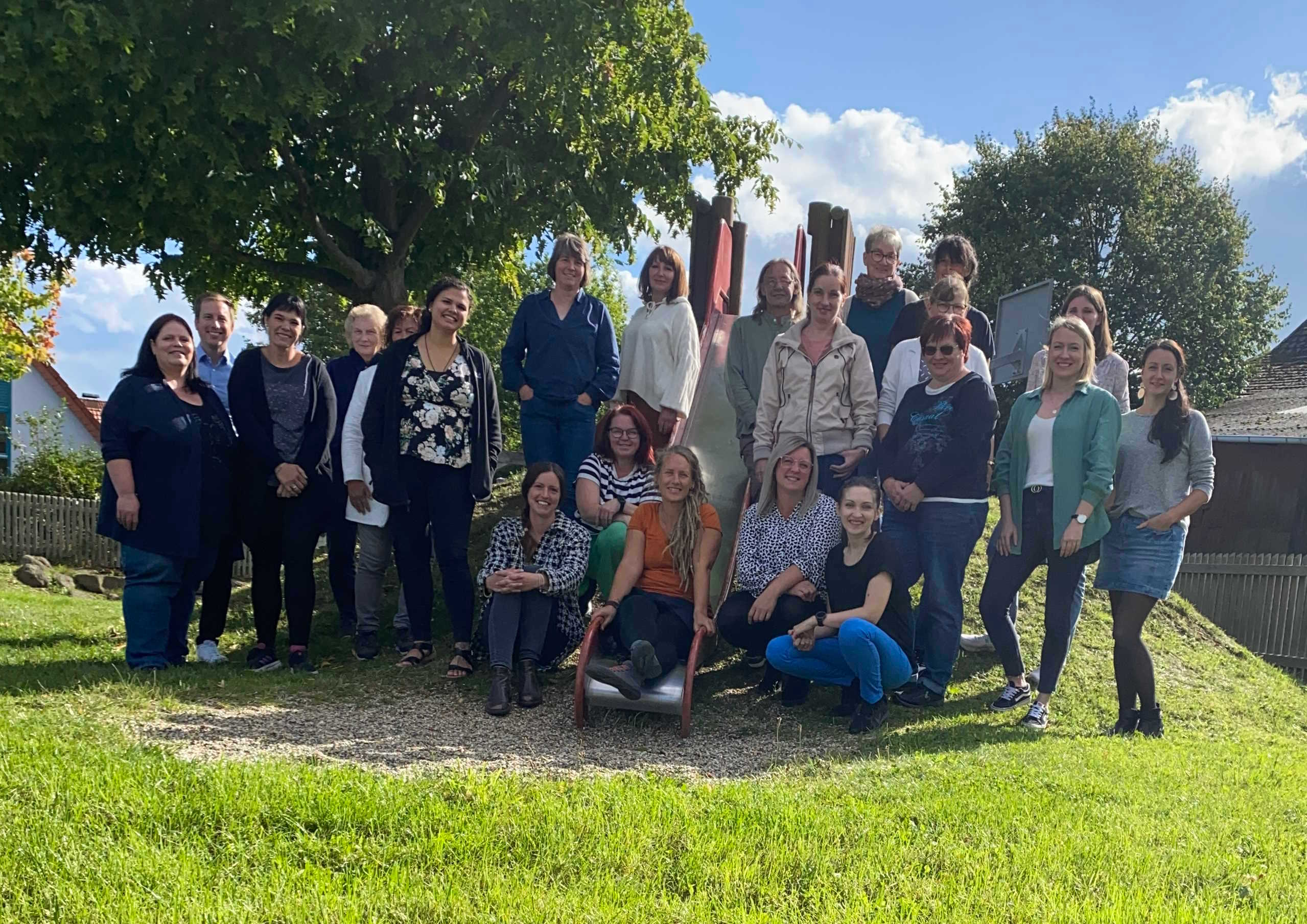 Eine Gruppe von etwa 40 Menschen hat sich auf einem mit Gras bewachsenem Spielplatzhügel zum Gruppenfoto aufgestellt. 