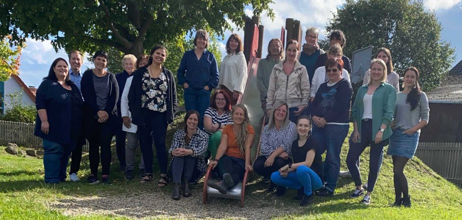 Eine Gruppe von etwa 40 Menschen hat sich auf einem mit Gras bewachsenem Spielplatzhügel zum Gruppenfoto aufgestellt. 