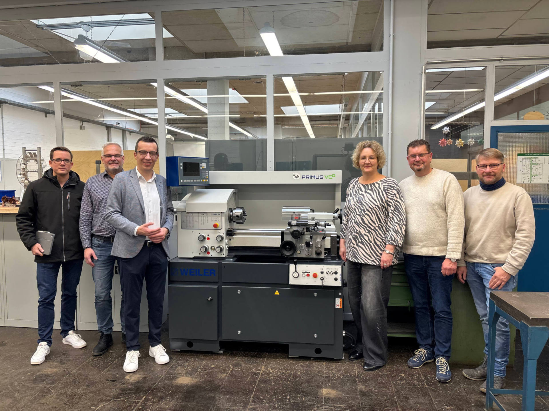 Sechs Personen haben sich an einer neuen Drehmaschine für ein Gruppenbild aufgestellt und lächeln in die Kamera.