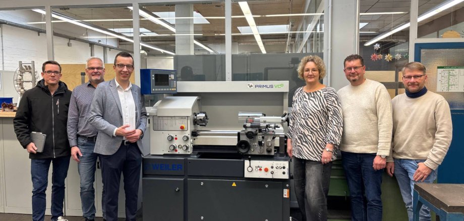 Sechs Personen haben sich an einer neuen Drehmaschine für ein Gruppenbild aufgestellt und lächeln in die Kamera.