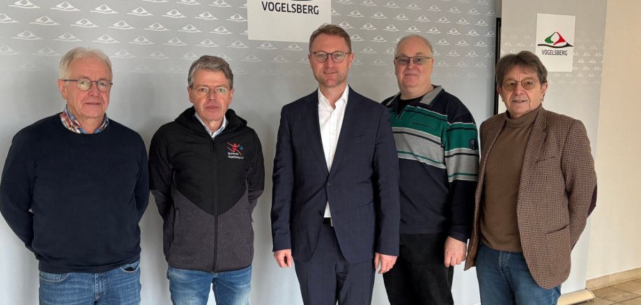 Fünf Personen stehen vor einer Fotowand und lächeln in die Kamera