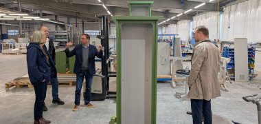 Mehrere Personen stehen in einer Produktionshalle um einen Schaltschrank herum.