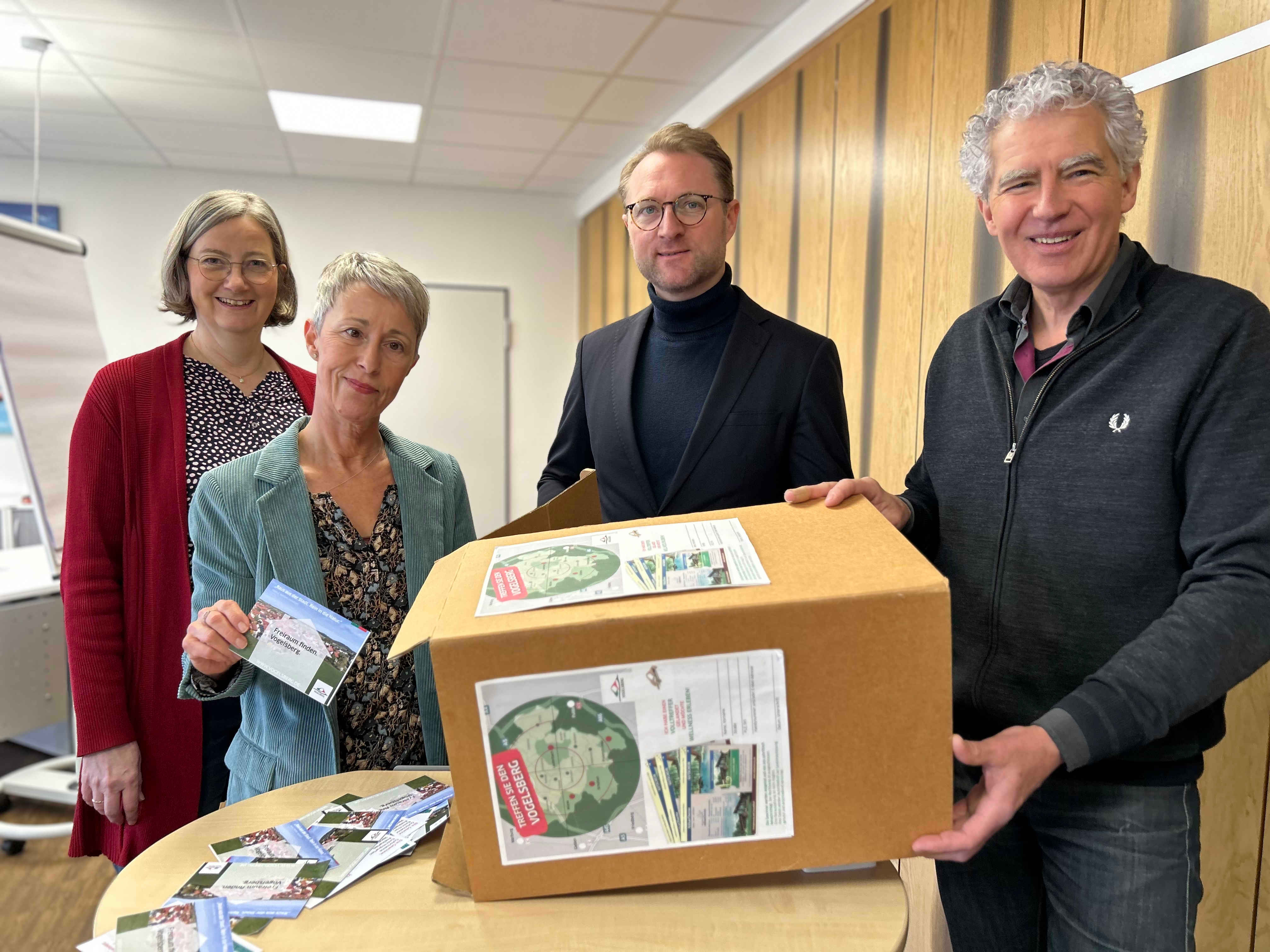 Vier Menschen stehen an einem kleinen Tisch und haben einen Karton mit Losen vor sich. 