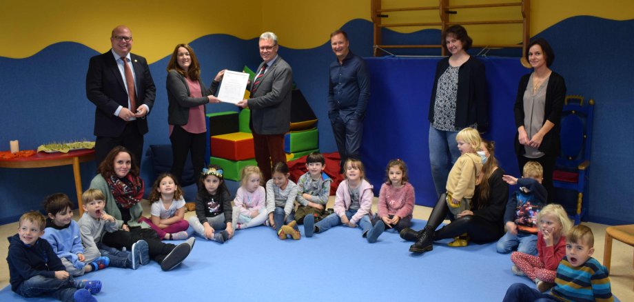 Gemeinsam mit Kindern in einer Kita. Überreicht  das Prädikatssiegel an die KiTa-Leitung: Dr. Dr. Rüdiger Rau (Dritter von links), gratuliert Nicole Weitzel (hinten, Zweite von links), zur Re-Zertifizierung. Auch Stephan Paule, Bürgermeister der Stadt Alsfeld (von links), Dr. Klaus Sayffaerth, Patenschaftszahnarzt der Einrichtung, Uta Born vom Arbeitskreis Jugendzahnpflege, und Sarah Schmick, vom KiTa-Elternbeirat, freuen sich über die Auszeichnung. 