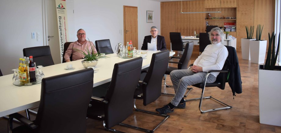 Landrat Manfred Görig verabschiedet Diplom-Sozialpädagoge und Sozialtherapeut Matthias Gold (rechts) in Ruhestand. Er war 40 Jahre beim Beratungszentrum Vogelsberg, zuletzt als Einrichtungsleiter, tätig.  Er übergibt an seinen Nachfolger Peter Pfeiffer. Sie sitzen an einem langen Tagungstisch  und schauen in die Kamera.