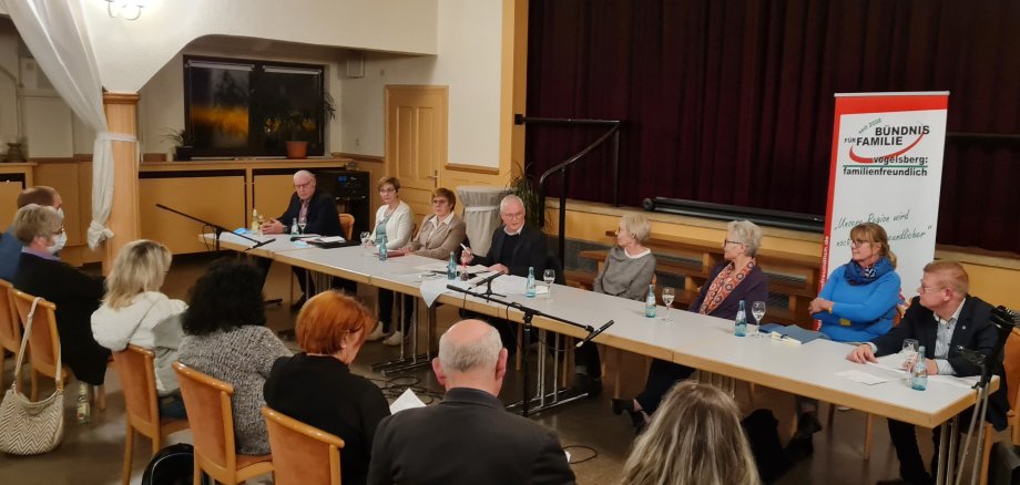 An einem langen Tisch sitzen acht Männer und Frauen. Sie nehmen als Experten an einer Podiumsdiskussion teil