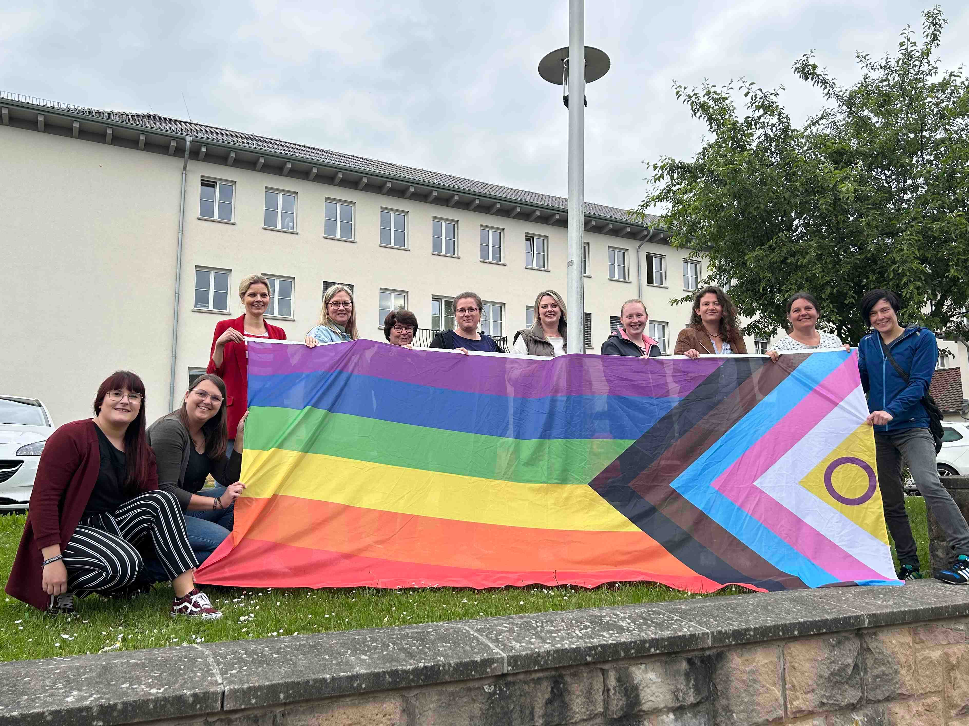 Gemeinsames Hissen der Pride-Progress-Flagge vor dem Gebäude der Kreisverwaltung des Vogelsbergkreises, als Zeichen gegen Diskriminierung von queeren Menschen: Hannah Müller (Sechste von links), Sachgebiet Jugendarbeit/Jugendbildung, Demokratieförderung im Jugendamt des Vogelsbergkreises, gemeinsam mit Antonia Schäfer (von links) und Sonja Hartmann, WIR-Vielfaltszentrum, der Frauenbeauftragten Elisabeth Lippert sowie Mitarbeiterinnen des Sachgebiets Jugendarbeit/Jugendbildung, Demokratieförderung. 