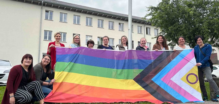 Gemeinsames Hissen der Pride-Progress-Flagge vor dem Gebäude der Kreisverwaltung des Vogelsbergkreises, als Zeichen gegen Diskriminierung von queeren Menschen: Hannah Müller (Sechste von links), Sachgebiet Jugendarbeit/Jugendbildung, Demokratieförderung im Jugendamt des Vogelsbergkreises, gemeinsam mit Antonia Schäfer (von links) und Sonja Hartmann, WIR-Vielfaltszentrum, der Frauenbeauftragten Elisabeth Lippert sowie Mitarbeiterinnen des Sachgebiets Jugendarbeit/Jugendbildung, Demokratieförderung. 