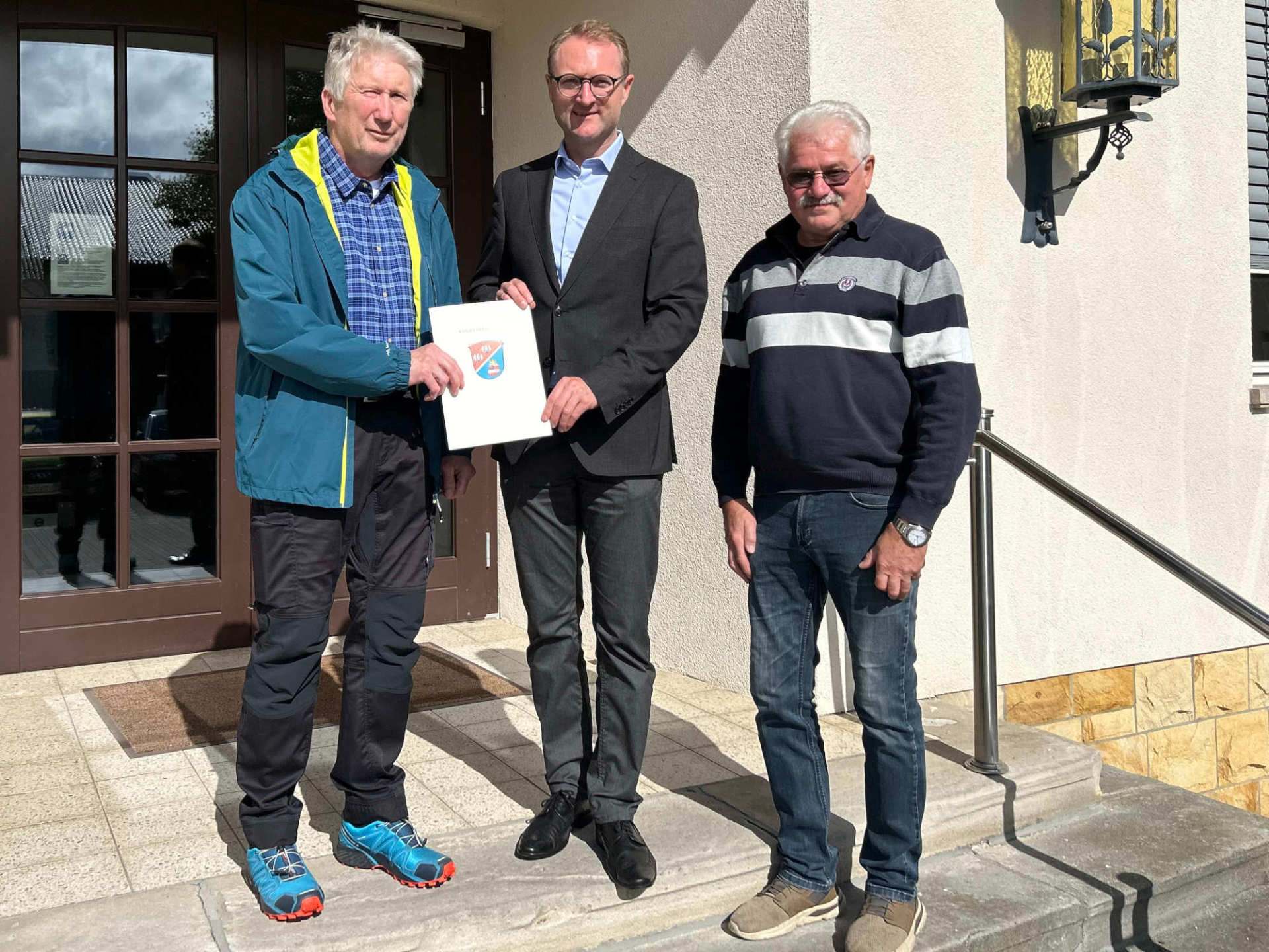 Landrat Dr. Jens Mischak (Mitte) übergibt Förderbescheid in Höhe von knapp 8.600 Euro an den Tennisclub Schotten: Schatzmeister Uwe Prihoda (links) und Gerhard Vogel, Platzwart und Technischer Leiter, freuen sich über die Förderung, die die Erneuerung des Dachs am Vereinsheim unterstützt.