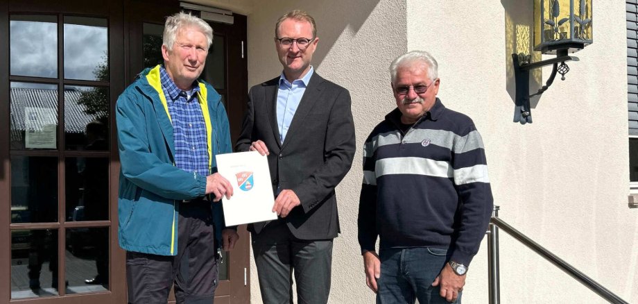 Landrat Dr. Jens Mischak (Mitte) übergibt Förderbescheid in Höhe von knapp 8.600 Euro an den Tennisclub Schotten: Schatzmeister Uwe Prihoda (links) und Gerhard Vogel, Platzwart und Technischer Leiter, freuen sich über die Förderung, die die Erneuerung des Dachs am Vereinsheim unterstützt.